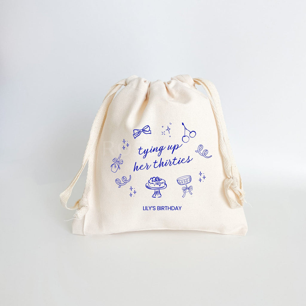 "Tying Up Her Thirties" with "Lily's Birthday" at the bottom with hand drawn birthday sketches on a cotton canvas drawstring bag with natural ribbon